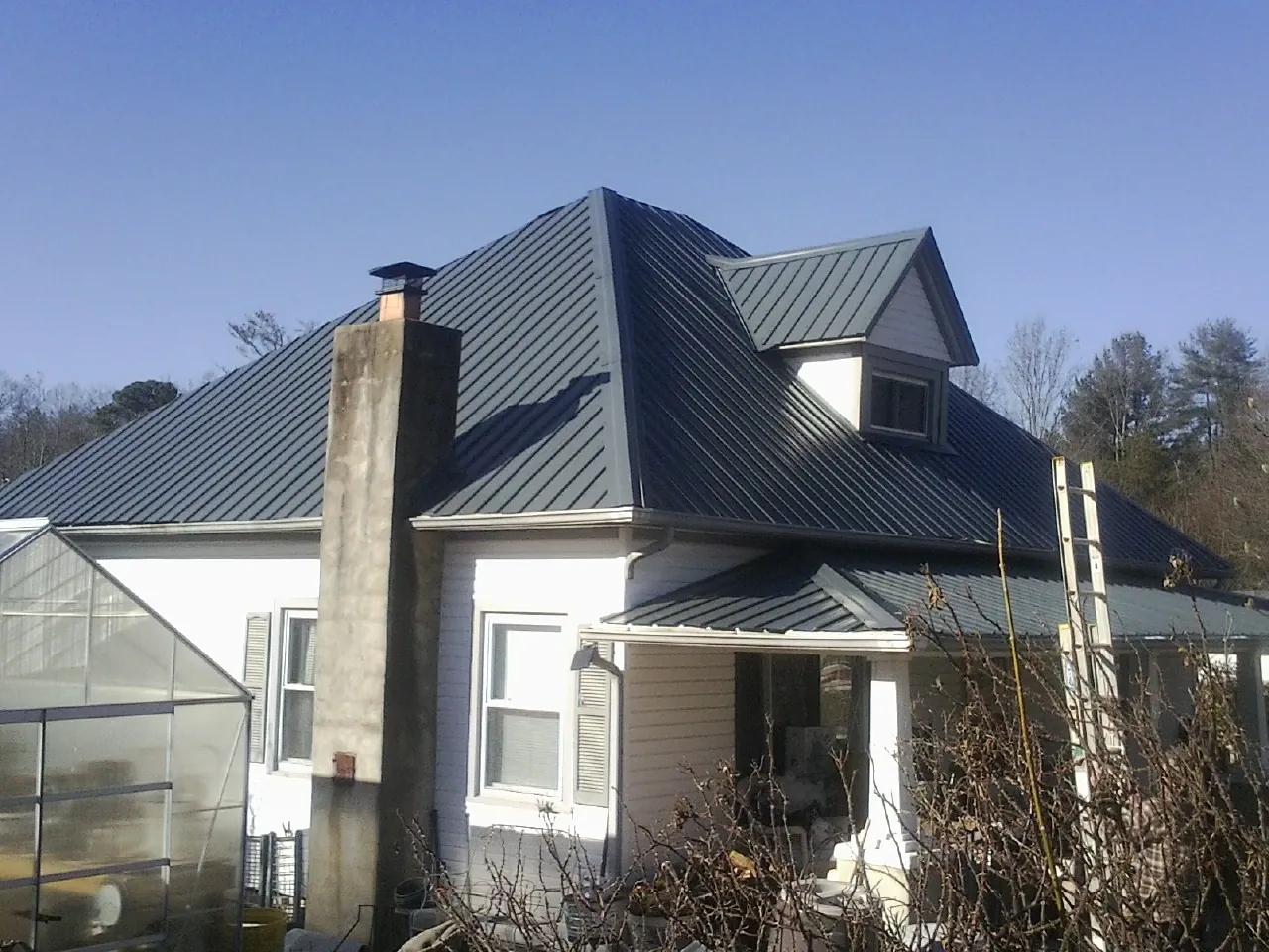 Dark blue standing seam metal roof on a white farmhouse with dormer — Slate & Tile Roof Repair by Roofing Brothers in Rural Hall
