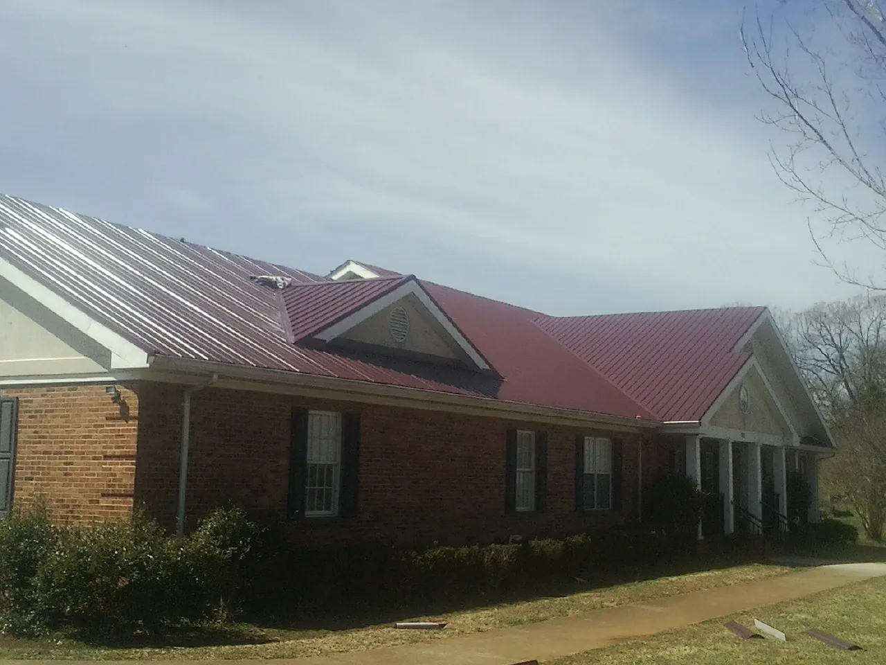 Red metal roof with gabled entries on a long brick building, from a Hail Damage Roof Repair job in Rural Hall