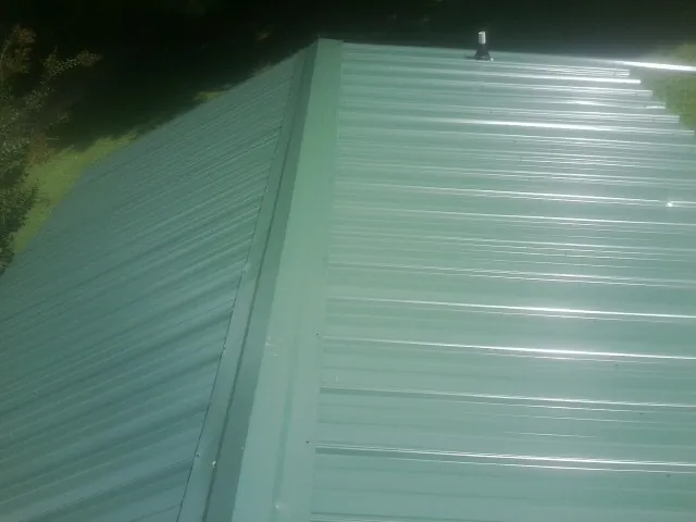 New green metal panels meeting at the ridge of a roof — Flat Roof Repair work by our crew in Rural Hall