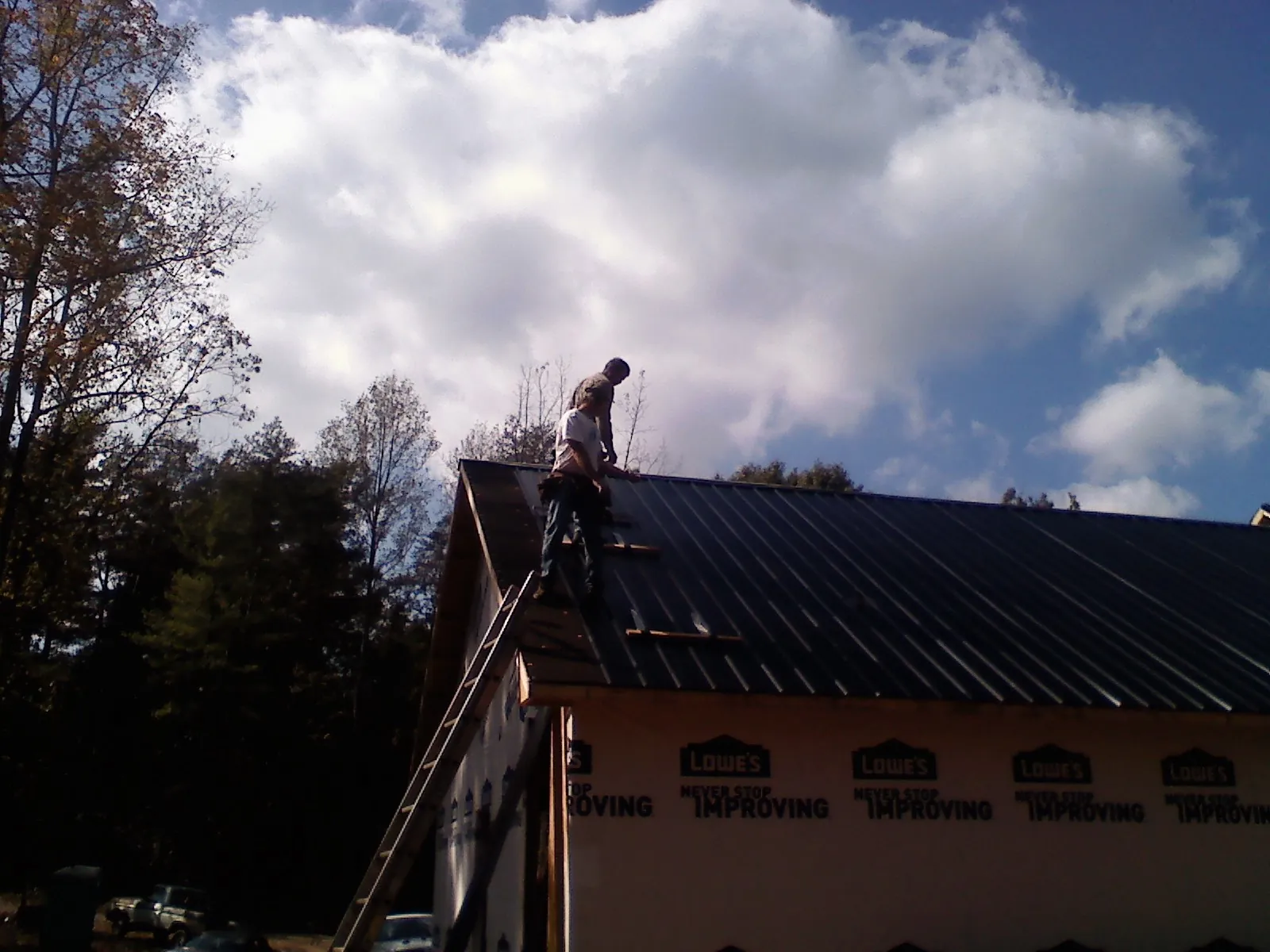 Roofer fastening dark metal panels high against a cloudy sky, from a Roof Inspection job in Rural Hall