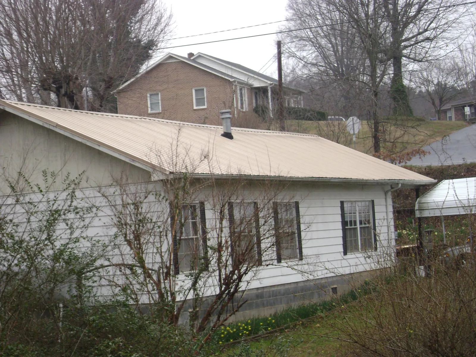 Tan metal roof on a white sided house set into a hillside — Commercial Roofing by Roofing Brothers in Rural Hall
