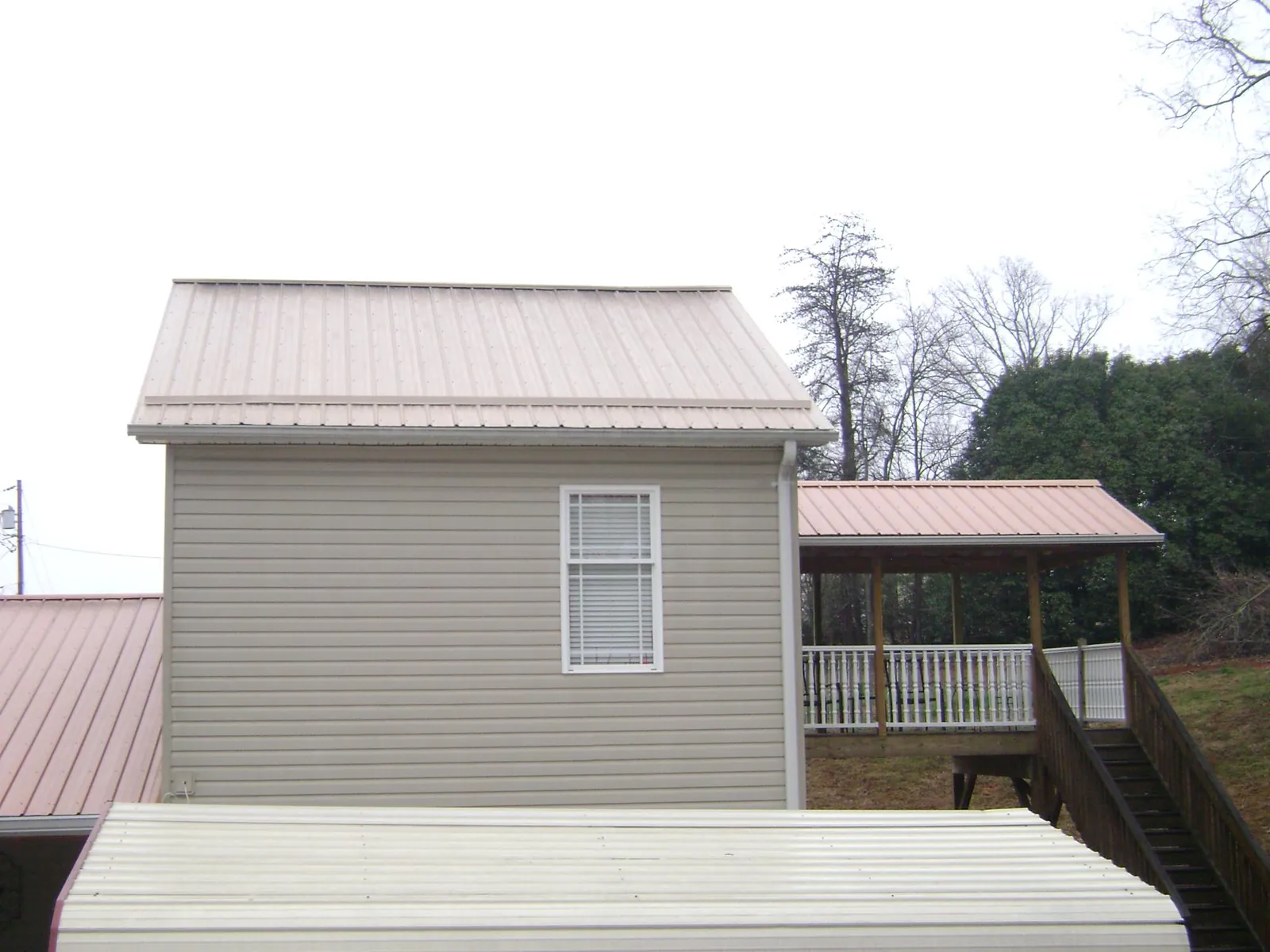 Tan metal roofs on a two story addition and attached porch, from a Roof Replacement job in Rural Hall